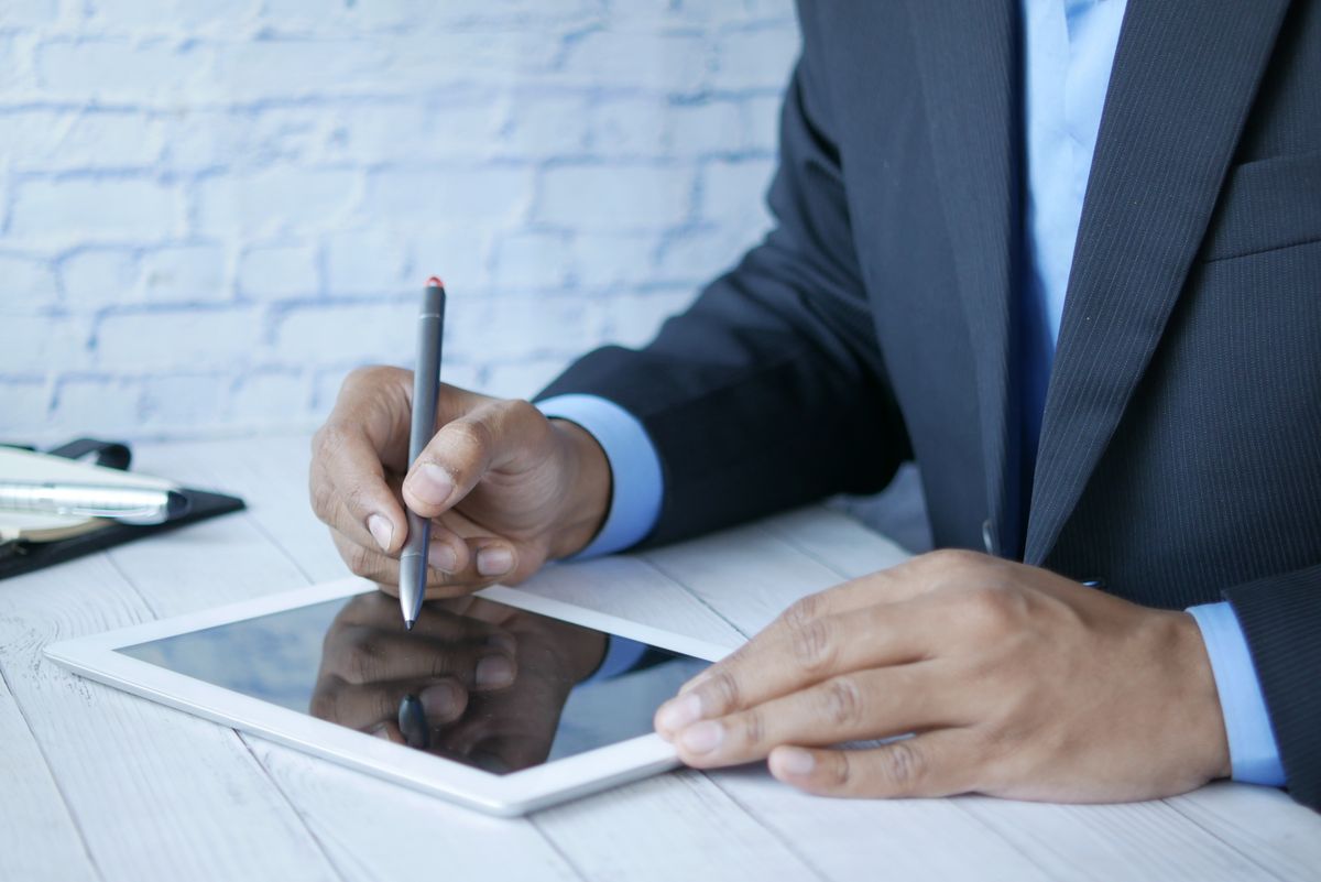 A person in a suit signing a document on a tablet with a stylus