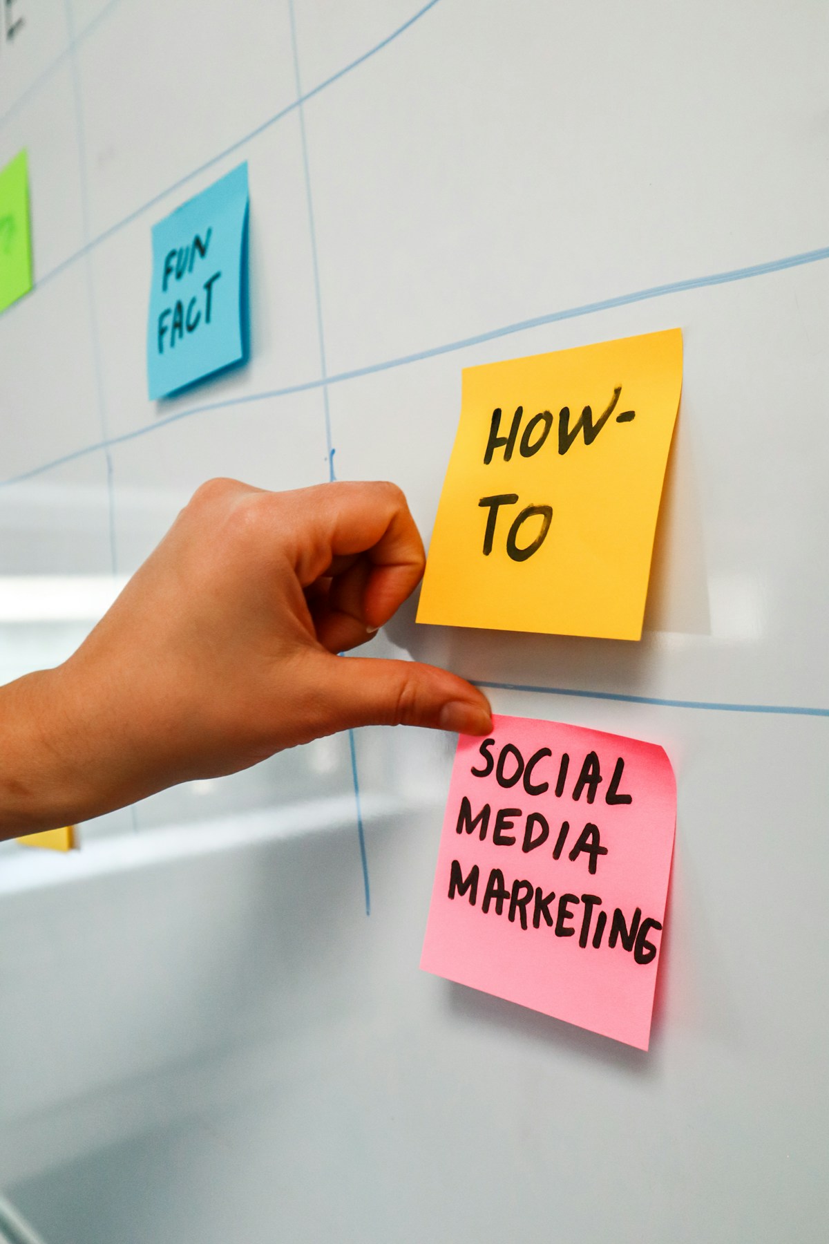 A hand placing sticky notes labelled &ldquo;social media marketing&rdquo; and &ldquo;how-to&rdquo; on a content-planning board